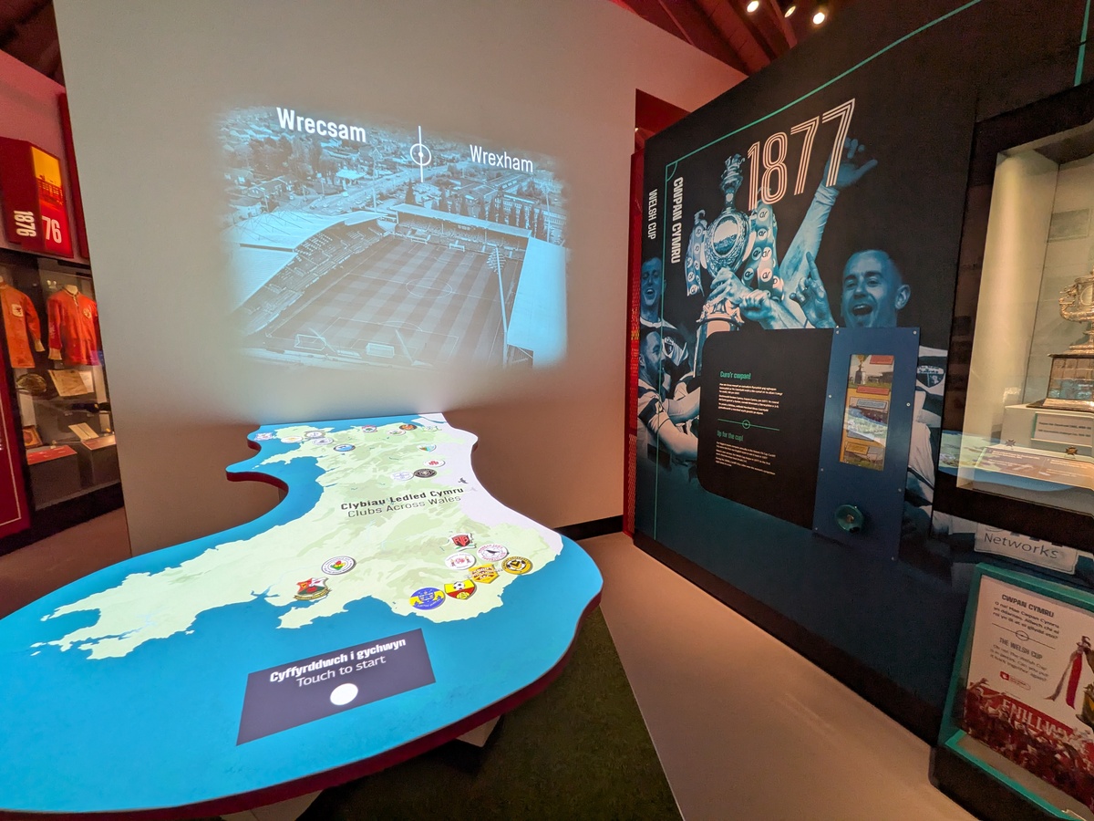Museum display with a lit map of Wales marked with club badges, and a projected football ground labelled Wrecsam and Wrexham